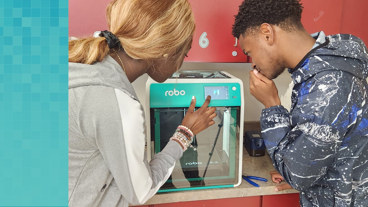 Two high school students program the print of their design on the touchscreen of the Robo E4 3D printer.